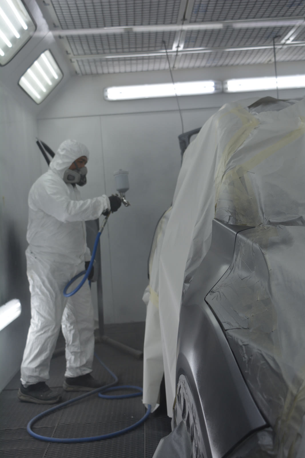 Técnico certificado aplicando pintura Sikkens en la cabina presurizada del taller